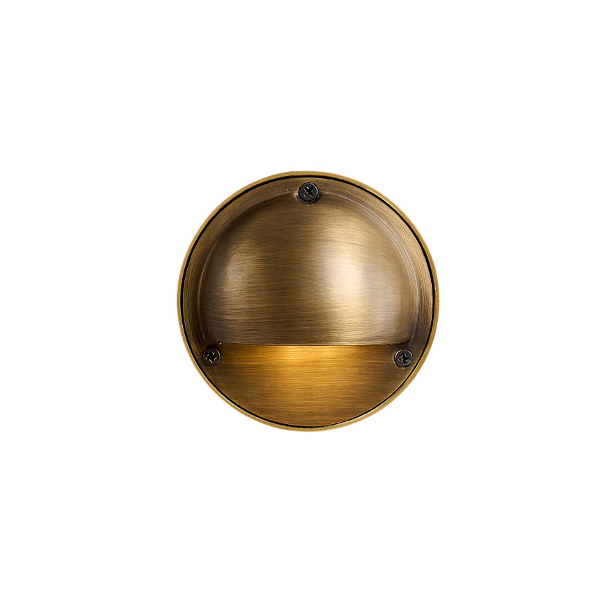 Compact weathered brass wall sconce with enclosed shade mounted on an indoor wall